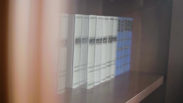 Man takes a book and puts her back on the shelf on the background of many rows of books on a wooden shelf in the library