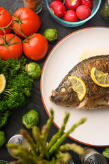 Tasty fish cooked with lemons on a background of fresh vegetables.Vertical frame