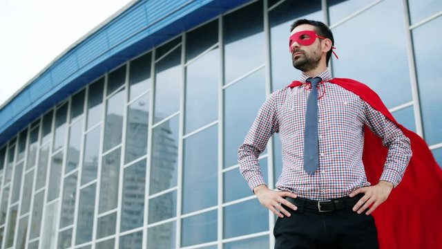 Portrait of ambitious man wearing red superhero mask and cape standing outdoors ready for big business in metropolis. People and achievements concept.