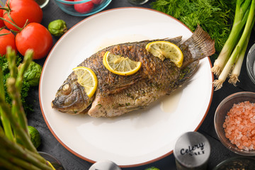 Eastern or European cuisine, Fried fish with fresh vegetables, on a wooden black background. I also eat healthy food. Seafood, recipe book, selling fish, restaurant business