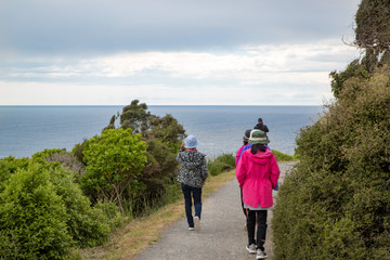 Asian tourists exploring New Zealand walk along the track to Nugget Point LIghthouse