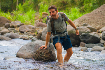 young happy and attractive man with travel backpack hiking in river at forest feeling free enjoying nature and fresh environment on summer trekking journey