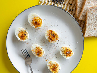 ฺBoiled egg topped with Cayenne pepper Pepper and Salt on a white dish,Egg colors white and yellow,Eat with bread