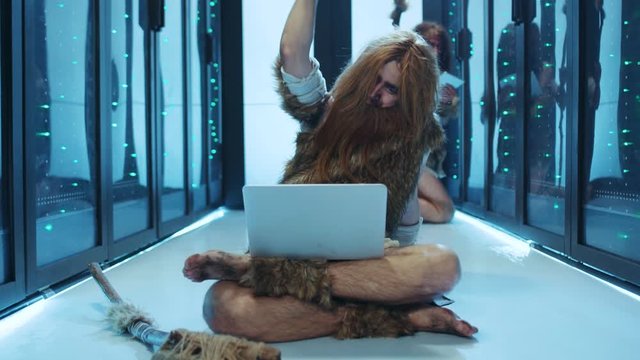 Primitive caveman of hunter-gatherers playing with laptop sitting on floor in database server. Tribe of wild nomadic neanderthals having fun with modern technology at data center.