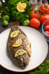 Tasty fish cooked with lemons on a background of fresh vegetables.Vertical frame