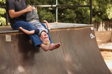 Father holding son upside down at skate park