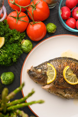 Cooked fish with ingredients, on black background. Vertical frame.