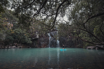 Young boy kayaking with paddle in cool blue water at Cedar Creek Falls near Airlie Beach in the Whitsundays, Queensland Australia