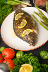 Tasty fish cooked with lemons on a background of fresh vegetables.Vertical frame