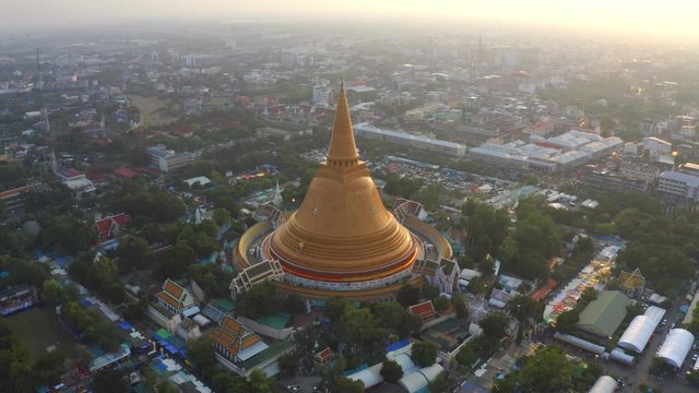 Aerial top view of Phra Pathommachedi temple at sunset. The golden buddhist pagoda with residential houses, urban city of Nakorn Pathom district, Thailand. Holy Thai architecture.