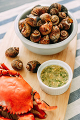 Grilled Laevistrombus Canarium in shells served with Thai spicy seafood sauce on wooden plates.
