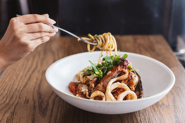 Hand pinching Spaghetti Seafood and lifted with a fork: Spaghetti with Prawns, Squids, Mussels Cooked in Olive Oil, Chillies and Garlic.