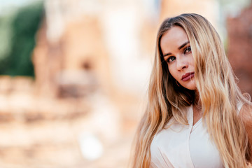 Portrait of beautiful blonde girl in white dress looking at camera while posing outdoors. Summer vacation, adventures concept. Horizontal shot.