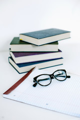 A stack of books and a blank notebook with glasses on it on a white background, home education