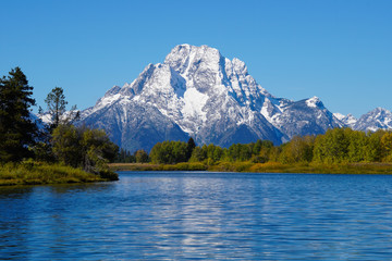 The Grand Tetons's Mount Moran rises majestically above the snake river and the forest's beautiful autumn colors.