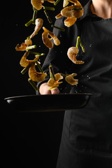 Chef cooks seafood, fry shrimps. Freezing in motion on a black photo, vertical photo