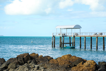 Small jetty by the beach with man fishing from boat underneath