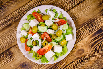 Ceramic plate with greek salad on wooden table. Top view