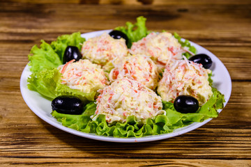 White plate with crab-cheese balls and lettuce leaves on wooden table