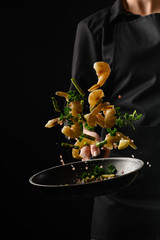Chef cooks seafood, fry shrimps. Freezing in motion on a black photo, vertical photo - 308623526