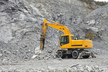 Wheel excavator with a hydraulic hammer breaks up large fragments of rock in a limestone quarry, close-up. Quarry equipment. Mining industry.