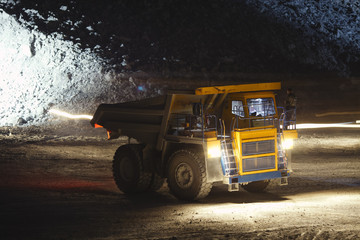 Heavy quarry dump truck stands in a quarry in the dark against the backdrop of smeared traces of moving light sources, close-up.
