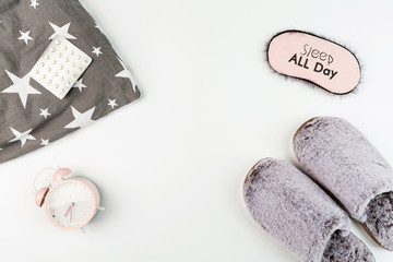 Flat lay with Soft fluffy slippers gray color, pillow, blindfold, pills and pink alarm clock isolated on white background. top view, overhead, mockup, template, copy space. Time for rest