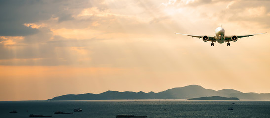 Passenger airplane. Landscape with Front of white airplane is flying in the orange sky with clouds over mountains, sea at colorful sunset. Passenger aircraft is landing. Commercial plane. Private jet