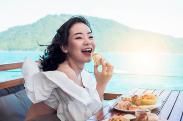 Beautiful woman is having breakfast beside blue sea and mountains