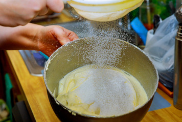Woman sifts the flour in mixer bowl with wipping eggs. Making cake dough.