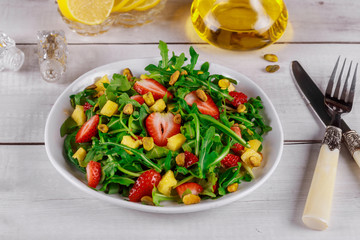 Fresh salad with arugula, strawberries, pineapple and pistachios served on white plate on rustic wooden table.