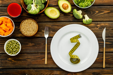Fototapeta na wymiar Diet program concept. Empty plate, measure tape and vegetables on dark wooden background top view