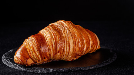 French cuisine concept. French croissant from puff pastry dough lies on a black slate board, on a black background. copy space