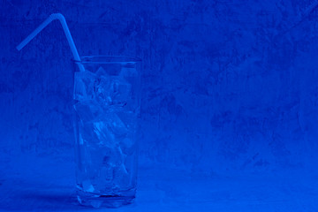 Empty tall glass with ice cubes and straw ready to pour cold summer beverage on cement background with copy space. Classic, blue monochrome, trend 2020