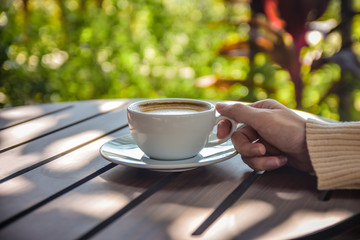 Close up hand holding cup of coffee on wooden table