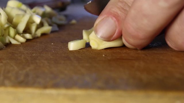 men's hands cut with a knife finely cloves of garlic on a wooden cutting Board