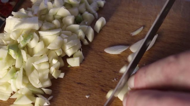 men's hands cut with a knife finely cloves of garlic on a wooden cutting Board