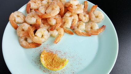 Shrimp served on a blue plate with lemon and red pepper.