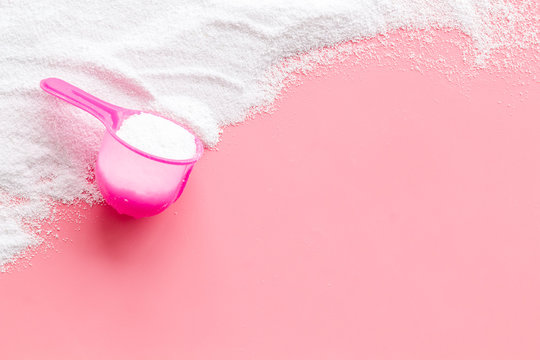 Washing powder in plastic spoon on pink background top view copy space