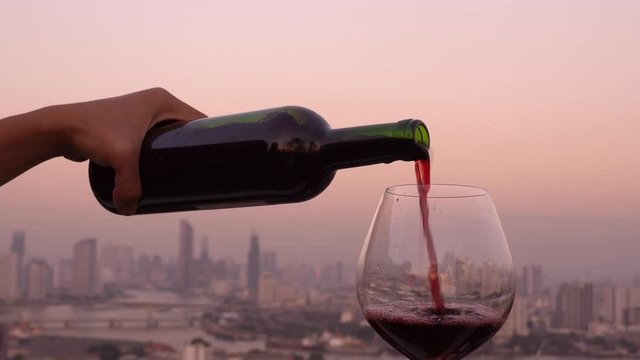 Young man which his hand Pouring red wine on the rooftop with city background , party concept