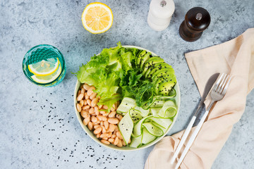 Vegetarian green salad bowl with fresh vegetables and canned white beans on a gray concrete background. Horizontal photo. Top view.