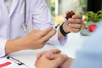 Doctor holding injection needle and vaccine bottle before treatment patient