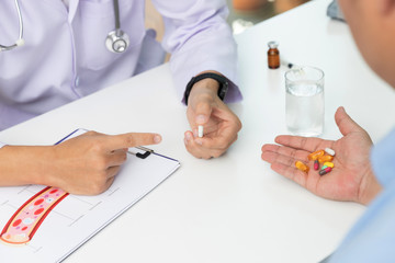 Doctor holding medicine pills in hand and explained medication  with assorted pharmaceutical medicine pills on table