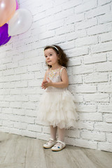 little cute girl is shy, standing near white brick wall at the feast