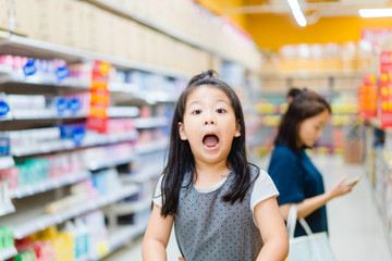 Surprised and excited face of happy little asian girl in supermarket with mom.Little girl open mouth in hypermarket with family.wow emotion in kid.