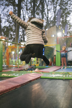 Girl with grey jacket jumping and playing on a stretch bed on a playground