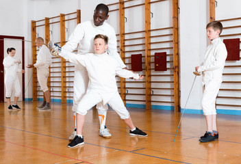 Focused boys fencers attentively listening to professional fencing coach in gym
