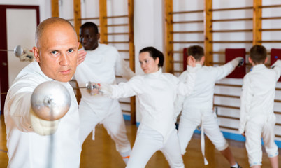 Adult man fencer practicing effective fencing techniques in training room