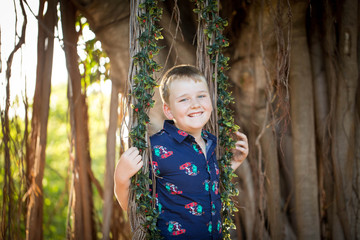 Pre-teen boy in Christmas outfit smiling while playing on fig tree swing covered in mistletoe 