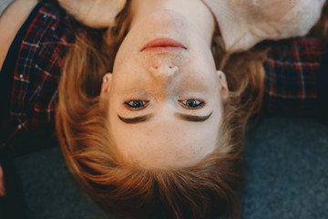 Close up top view portrait of a lovely young woman with red hair and freckles looking at camera smiling while leaning on a bed at home.